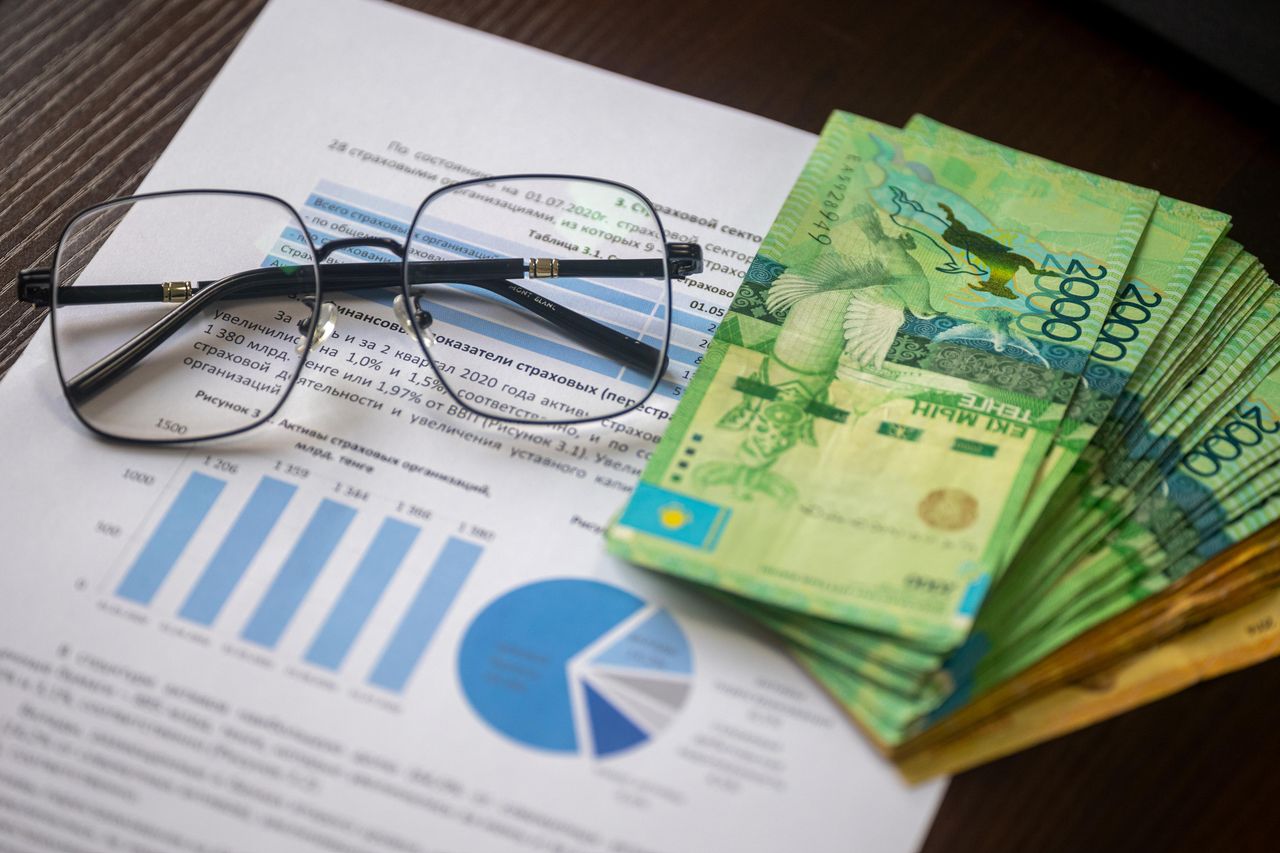 Kazakhstani tenge notes and financial reports on a desk, depicting financial analysis.